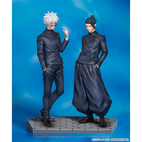 Figures of Satoru Gojo and Suguru Geto from Jujutsu Kaisen. Gojo is on the left with white spiky hair and blue-tinted glasses, wearing a dark outfit, while Geto is on the right with his hair tied up in a bun, dressed in a similar dark high-necked outfit, both standing against a blue sky background